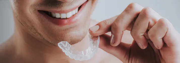 Orthodontist West Chester PA Retainers Patient holding clear retainers next to his mouth while smiling